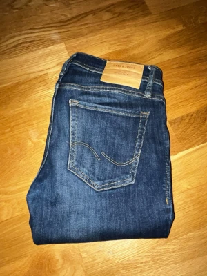 Mörkblå jeans från Jack & Jones - Snygga mörkblå jeans från Jack & Jones med klassisk femficksdesign och kontrastsömmar. Jeansen har en rak passform och är tillverkade i mjukt denimtyg med en läderpatch bak i midjan. Perfekta för en avslappnad och stilren look.