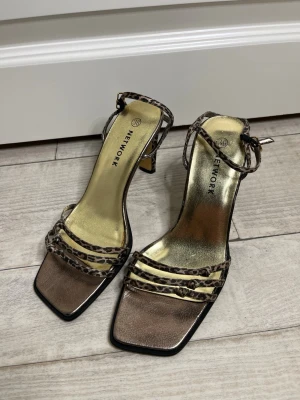 Leopardmönstrade pumps från Network - Snygga pumps i storlek 36 men passar 37  med leopardmönstrade remmar och fyrkantig tå från Network. Skorna har guldfärgad innersula och smal klack. Materialet ser ut att vara konstläder med metallicfinish. Perfekta för dig som vill sticka ut med ett trendigt djurmönster.