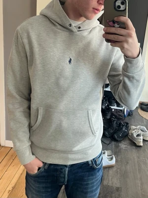 Ljusgrå hoodie från Ralph Lauren - Kolla in mina andra plagg!!  Snygg ljusgrå hoodie från Ralph Lauren med klassisk broderad logga på bröstet. Hoodien har huva med dragsko och en stor magficka framtill. Hoodien är i väldigt bra skick saknar bara snören.