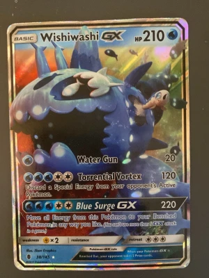 Wishiwashi GX Pokémonkort holografiskt - Säljer ett holografiskt Wishiwashi GX Pokémonkort med färgstark design och metallic-effekt. Kortet har HP 210 och attacker som Water Gun, Torrential Vortex och Blue Surge GX. Märkt med nummer 38/145 och tillverkat av Pokémon Company.