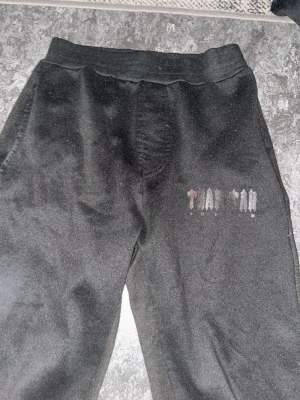 Svarta mjukisbyxor Trapstar London - Svarta mjukisbyxor från Trapstar London med tryckt logga på ena benet. Byxorna har resår i midjan och är tillverkade i mjukt material som passar perfekt för en avslappnad stil. Snygga att matcha med hoodie eller t-shirt.