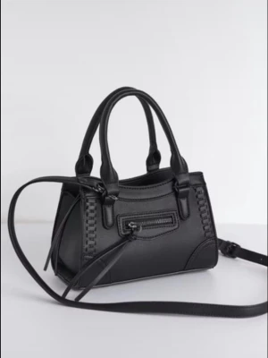 Svart handväska med axelrem - Snygg svart handväska i konstläder med både handtag och avtagbar axelrem. Väskan har en liten dragkedjeficka framtill och dekorativa sömmar längs kanterna. Perfekt storlek för det viktigaste och stilren design som passar till många outfits.