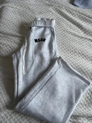 Grå mjukisbyxor från Missguided - Snygga ljusgrå mjukisbyxor från Missguided med svart MSGD-tryck på ena benet. Byxorna har resår och dragsko i midjan samt mjukt material i bomull. Perfekta för en chill och avslappnad stil.