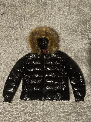 vet ej - Glansig svart pufferjacka med huva med päls. Nästan aldrig använd och pälsen går även att ta av. Står XL i kvinnostorlek så skulle säga typ S i herr. Hör av er om ni har frågor😁