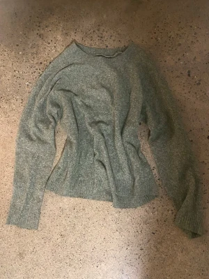 Grågrön stickad tröja med rund hals - Mysig stickad tröja i en grågrön nyans med rund halsringning och långa ärmar. Tröjan har en avslappnad passform och ribbstickade muddar vid ärmslut och nederkant. Perfekt för lager-på-lager och chill dagar.