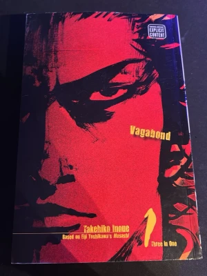 Vagabond Volym 1 VizBig Edition - Säljer manga-boken Vagabond Volym 1 av Takehiko Inoue, VizBig Edition. Omslaget är rött och svart med en intensiv illustration av huvudkaraktären. Boken är en samlingsvolym (Three in One) och baseras på Eiji Yoshikawas Musashi.