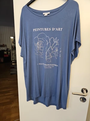 Blå oversized t-shirt från Amisu - Blå oversized t-shirt från Amisu med silvrigt tryck framtill som föreställer blommor och text .              T-shirten har korta ärmar och en lös passform, perfekt för en avslappnad stil.