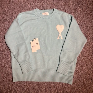 Ljusblå stickad tröja från Ami Paris storlek S - Superfin ljusblå stickad tröja från Ami Paris med vitt hjärta och A på bröstet. Tröjan har lång ärm, ribbade muddar och en avslappnad passform. Perfekt för dig som gillar stilrena och trendiga plagg. Pris kan diskuteras 😊