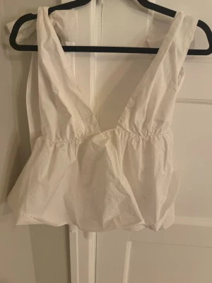 Vit croppad topp med v-ringning Zara  - Säljer en vit croppad topp med breda axelband och djup v-ringning både fram och bak. Toppen har en luftig och lätt passform med rynkade detaljer under bysten. Perfekt för sommaren och enkel att styla till olika outfits. Jättefin till sommaren. Knappt använd 