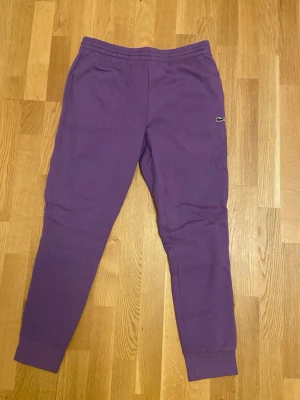 Oanvända lila Lacoste Mjukisbyxor (Nyskick) - Säljer ett par riktigt snygga och helt oanvända mjukisbyxor från Lacoste i en unik lila färg. De är endast provade och skicket är 10/10. De passar både M och L. Nypris: 1200kr