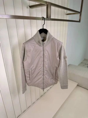 Beige cardiganjacka från Moncler - Snygg beige cardiganjacka från Moncler med stickade ärmar och krage samt quiltad front i glansigt material. Jackan har dragkedja framtill, ribbade muddar och två fickor. Moncler-logga på ärmen ger en exklusiv touch.