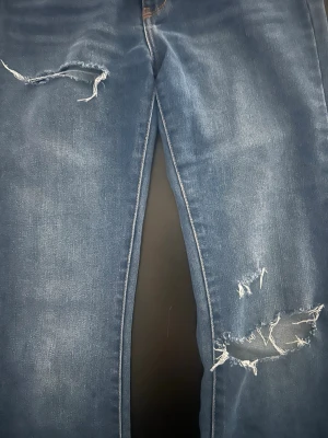 Levi's blåa Jena’s med hål  - Blå jeans från Levi's med klassisk femficksdesign och röd Levi's-tag på bakfickan. Jeansen har raka ben och slitna detaljer med hål på knäna för en trendig look. Perfekta för dig som gillar en avslappnad och cool stil. Nu pris 600