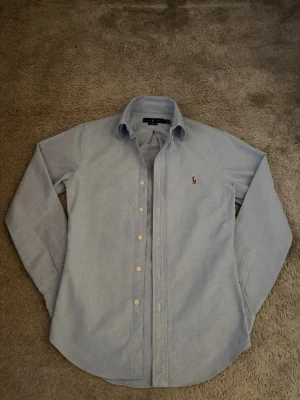 Ralph Lauren skjorta - Säljer en riktigt snygg ljusblå skjorta från Ralph Lauren i storlek XS( passar dig mellan 155-172 cm). Den är i väldigt bra skicka, har bara haft den 2-3 gånger. Skriv gärna om du har några frågor!