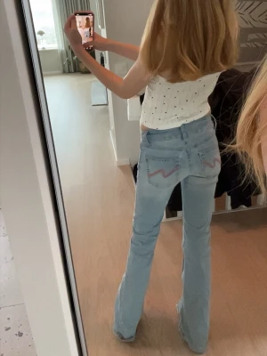 Ljusblå bootcut jeans från 7 For All Mankind - Säljer ett par ljusblå bootcut jens med låg midja och klassiska fickor. Jeansen har den ikoniska broderade detaljen på bakfickorna och är Perfekta för en avslappnad och trendig look.