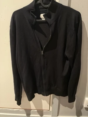  merinoullskofta från These Glory Days - Säljer en mörkblå kofta från These Glory Days i mjuk och exklusiv merinoull. Koftan har dragkedja framtill och en stilren, enkel design som passar perfekt till lager på lager. Långärmad och riktigt skön att bära under kyligare dagar. Storleken är 39-40/ Medium.