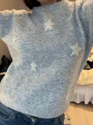Ljusgrå stickad tröja med stjärnor - Mysig ljusgrå stickad tröja med vita stjärnor som mönster. Tröjan har rund halsringning, långa ärmar och ribbade muddar vid ärmslut och nederkant. Storlek 152 men skulle säga att den passar xxs-s