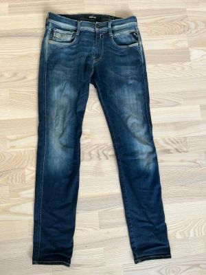 Mörkblå slim fit jeans från Replay - Snygga mörkblå slim fit jeans från Replay med slitningar och ljusare partier på låren. Klassisk femficksmodell med dragkedja och knapp. Tydliga kontrastsömmar och Replay-logga. Storlek 30/32