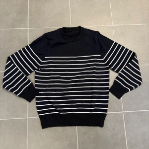 Mörkblå randig tröja - Snygg mörkblå tröja med vita horisontella ränder. Tröjan har rund halsringning, långa ärmar och ribbade muddar vid ärmslut och nederkant. Perfekt för en stilren och avslappnad look.