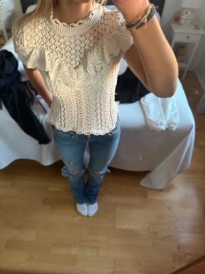 Vit spetsblus med volangdetalj - Supersöt vit spetsblus med korta ärmar och volangdetalj över bröstet❣️Blusen har ett virkat mönster och rund halsringning. Nästan aldrig använd