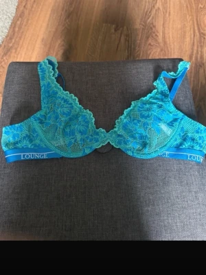 Blå spets-bh från Lounge - Snygg blå bh från Lounge med spetsdetaljer och blommigt mönster. Bh:n har justerbara axelband och elastiskt band med Lounge-logga under bysten. Perfekt för dig som gillar en feminin och trendig stil.