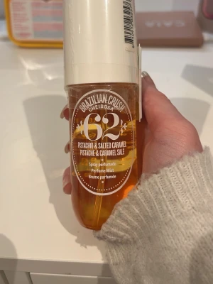 Brazilian Crush Cheirosa 62 Perfume Mist - En doftmist från Sol de Janeiro, Brazilian Crush Cheirosa 62, med noter av pistage och saltad karamell. Flaskan är genomskinlig med guldfärgad vätska och vitt lock. Perfekt för dig som gillar söta och krämiga dofter. Helt ny, aldrig öppnad.