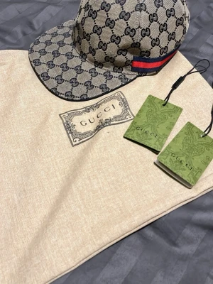 Gucci GG Supreme keps beige - Säljer en beige Gucci keps i GG Supreme canvas med klassiskt monogrammönster och röd-blå rand på sidan. Justerbar rem baktill i svart läder. Kepsen har böjd skärm och kommer med originalpåse och tags.