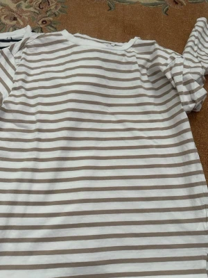 Två långärmade tröjor i stl S - Två långrandiga tröjor, en med beiga streck och en med svarta. Tillverkad i 100% bomull för en mjuk och skön känsla. Perfekt till jeans eller kjol och har en klassisk, avslappnad passform med rund hals. Fint begagnat skick! 