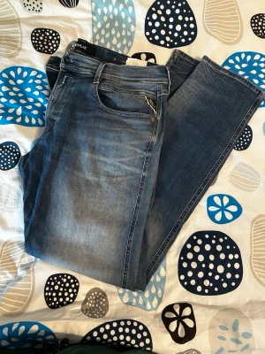 Blå raka jeans från Replay - Snygga blå jeans från Replay med klassisk femficksmodell och raka ben. Jeansen har en lätt tvättad look och detaljerade sömmar. Perfekta för dig som gillar en avslappnad men stilren vibe. Tillverkade i bomull för skön känsla.