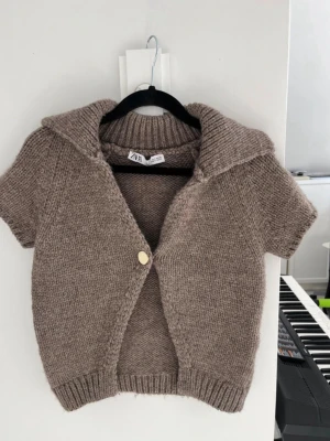 Beige stickad kofta från Zara💕 - Kortärmad stickad kofta från Zara i beige nyans. Koftan har en bred krage, en knapp framtill och ribbade muddar vid ärmslut och nederkant. Perfekt att slänga över en topp för en chill look.✨✨✨❤️❤️