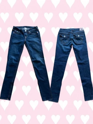 Mörkblå low rise jeans från True Religion - Snygga mörkblå low rise jeans från True Religion i modellen Julie. Jeansen har låg midja och smal passform. Storlek W31. Nypris cirka 1300kr. Väldigt bra skick. Byxorna har en liten fläck på ena benet som går bort i tvätten. Skriv om du har några frågor! Priset går att diskutera!