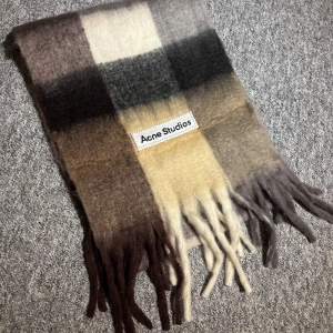 Rutig halsduk från Acne Studios  - Supermjuk och fluffig halsduk från Acne Studios i rutigt mönster med nyanser av brunt, beige, grått och svart. Halsduken har fransar i ändarna och en tydlig logotypetikett. Perfekt för att lyfta din outfit med en trendig touch. Pris kan diskutera. Fri Frakt nu!! 🚚 😊
