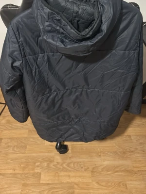 Sail racing jacka  - Med rätt tvätt kan se ny ut.Mörkblå dunjacka från Sail Antarctica med huva och dragkedja framtill. Jackan har en svart bröstficka med dragkedja och logga på vänster sida. Perfekt för kalla dagar och har en sportig look.