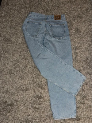 Ljusblå sweetsktbs jeans  - Säljer ett par ljusblå jeans från Junkyard 30/30 med klassisk rak passform och hög midja. Jeansen har två bakfickor och en snygg läderpatch med logga bak i midjan. Tillverkade i slitstark denim som ger en tidlös look.