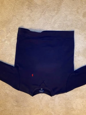 Mörkblå sweatshirt från Polo Ralph Lauren - Klassisk mörkblå sweatshirt från Polo Ralph Lauren med röd broderad logga på bröstet. Tröjan har rund halsringning och långa ärmar. Tillverkad i mjukt bomullsmaterial för en bekväm känsla.