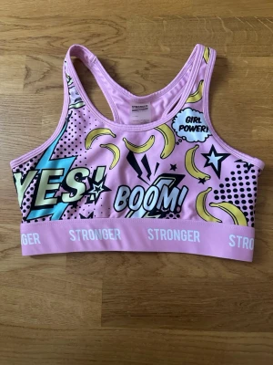 Rosa sport-bh från Stronger - Färgglad sport-bh i rosa med serietidningstryck. Jag säljer även de matchande tightsen.            Helt ny.                                                                                  Ordinarie pris:499kr