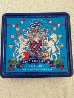 McVitie's King Charles III kakburk - Snygg blå plåtburk från McVitie's med motiv av lejon och enhörning, designad för King Charles III:s kröning i maj 2023. Innehåller ett urval av olika kakor som Digestives, Bourbon Creams och Jam Ring. Perfekt samlarobjekt eller present till kakälskare.