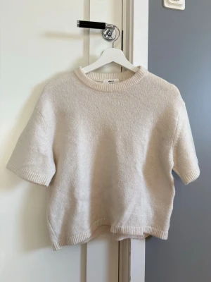 Vit kortärmad stickad tröja från Gina Tricot - En stilren vit stickad tröja med korta ärmar och rund hals. Tröjan har ribbade muddar vid ärmslut och nederkant.