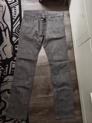 Grå raka jeans från D - Säljer ett par grå jeans från D med rak passform och klassisk femficksdesign. Jeansen har en diskret röd D-logga vid gylfen och är tillverkade i ett slitstarkt denimtyg. Perfekta för en stilren och avslappnad look.