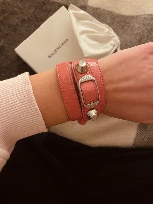 Rosa Balenciaga läderarmband - Säljer ett rosa Balenciaga armband i läder med dubbla remmar och silverfärgade nitar och spänne. Kommer med original ask och dustbag. Man kan ändra armbandets storlek i tre steg. Den är i väldigt bra skick förutom lite små slitningar vid spännet men det är inget märkbart när man har på sig det!🩷