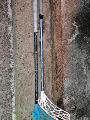 Unihoc Titan Series innebandyklubbor - Två Unihoc Titan Series innebandyklubbor med svart och grått skaft samt evolite blad i vitt och turkost(PEplast) Klubborna har ett modernt grafiskt mönster och är tillverkade i lätt material, perfekta för innebandyträning eller match. 96cm långa skaft. Jag har förlängt dom så att dom nu är 101cm långa. (Men förlängningen går att ta bort om man vill.)