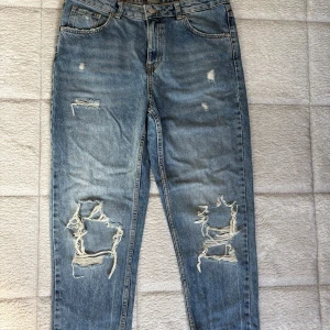 Blå ripped jeans med raka ben - Snygga blå jeans med raka ben och slitna detaljer på både fram- och baksida. Jeansen har klassisk femficksdesign, hög midja och råa benslut. Perfekta för en avslappnad streetstyle-look.