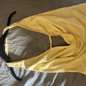 Gul halterneck tubtopp - Säljer en ljusgul halterneck tubtopp med snygg drapering framtill och öppen rygg. Toppen är ärmlös och har en enkel, stilren design. Tillverkad i mjukt bomullsmaterial. Snygg och fin fest topp