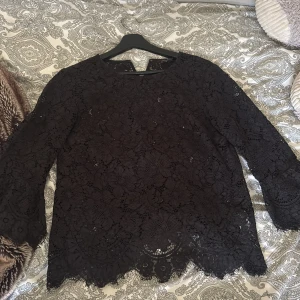 Svart spetsblus från Banana Republic - Supersnygg svart blus från Banana Republic i spets med blommigt mönster. Blusen har trekvartsärmar med lätt utsvängd kant och fina detaljer längs nederkanten. Perfekt för dig som gillar en elegant och trendig look.