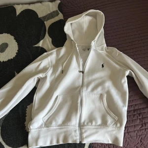 Vit hoodie från Polo Ralph Lauren - Säljer en stilren vit hoodie från Polo Ralph Lauren med dragkedja och huva. Tröjan har två fickor framtill och den klassiska broderade loggan på bröstet. Perfekt för dig som gillar en clean och enkel look. Inprincip som ny! pris ej hugget i sten
