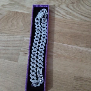Blingigt silverfärgat armband - Säljer ett chunky armband i silverfärg med stora länkar täckta av glittrande stenar. Armbandet har en bred design och ett lås dekorerat med små stenar för extra bling. Perfekt för dig som vill sticka ut och addera lite extra shine till din stil.