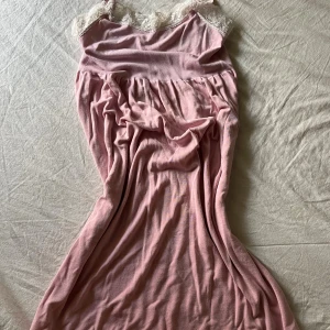 Rosa klänning med spetsdetalj - Söt rosa klänning med mjukt fall och vacker vit spets upptill vid halsringningen. Klänningen har en romantisk känsla och är ärmlös med en avslappnad passform. Perfekt för dig som gillar feminina och bekväma plagg.