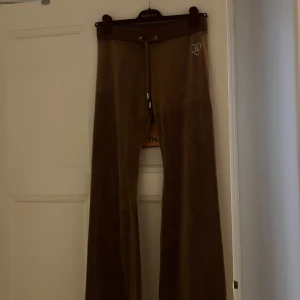 Bruna velourbyxor Juicy Couture S - Bruna velourbyxor från Juicy Couture med snörning i midjan och strassdetaljer. Byxorna har bootcut-modell, broderat JC-hjärta fram och glittrande 'JUICY' på baksidan. En gammal snygg modell lite för långa för mej som är 158 men hoppas dem passar någon annan som faktiskt kommer använda dem!