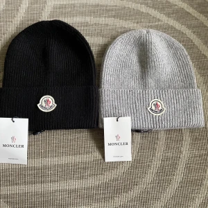 Moncler mössa svart och grå - Snygg  mössa från Moncler. Finns i svart och ljusgrått, Perfekt accessoar för kyliga dagar. Tillverkad i mjukt ullmaterial för extra komfort. Säljer en för 300kr och båda två för 525