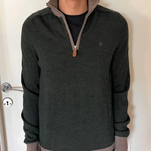 Grön merinoullströja från Morris - Mörkgrön stickad tröja från Morris i 100% merinoull med beige ribbade muddar och krage. Tröjan har half zip-dragkedja och diskret Morris-logga broderad på bröstet. Perfekt för lager-på-lager och snygg till jeans.