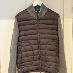 Grå moncler cardigan - Snygg grå cardiganjacka från Moncler med quiltad front och stickade ärmar samt rygg. Jackan har hög krage, dragkedja framtill och två fickor med dragkedja. Perfekt för höst. Har ej kvitto på jacken men är köpt för 3500kr. Storlek är M men passar S. Jackan är äkta och har NFC märke. Hör av dig om du är intresserad och vill ha fler bilder. På den högra sidan så har jackan sprätt upp lite därför priset.Priser är inte hugget i sten!